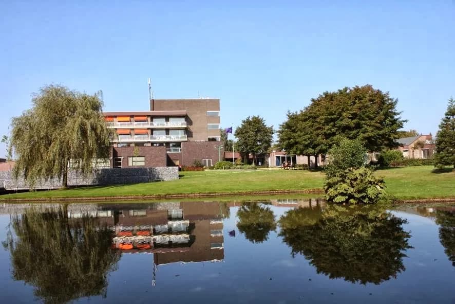 Gebouw van MST Haaksbergen aan het water, met grasveld en bomen