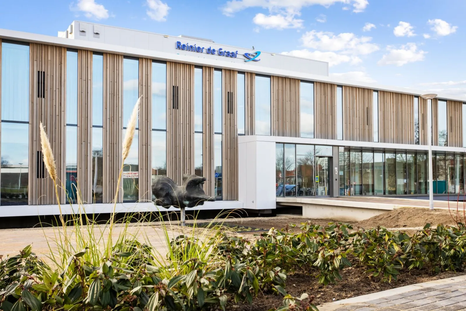 Behandelcentrum Voorburg van Reinier de Graaf met lichte gevel met houten lamellen, glazen pui en beeld in de voortuin