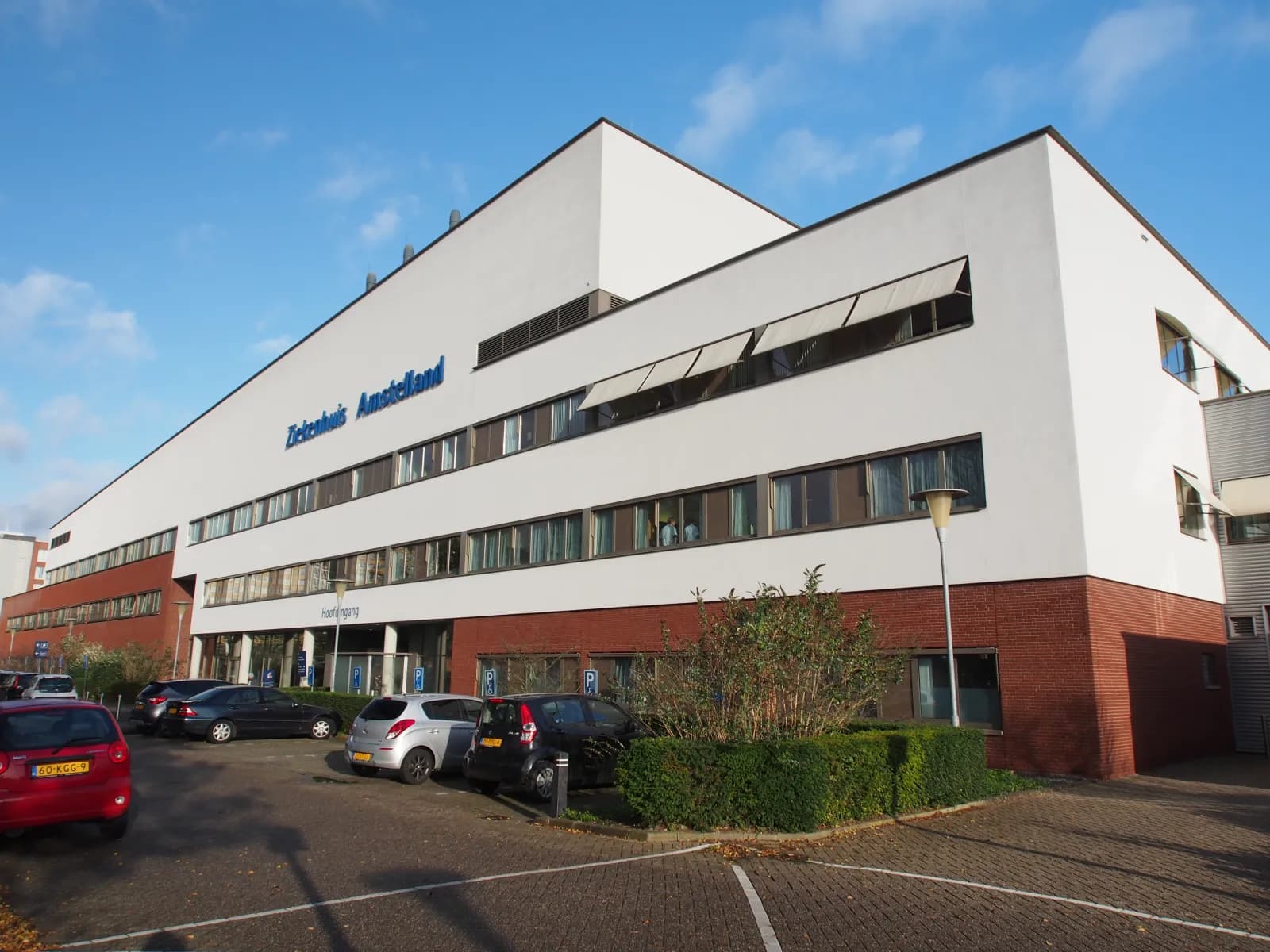 Wit gebouw van Ziekenhuis Amstelland met de naam op de gevel en het parkeerterrein ervoor
