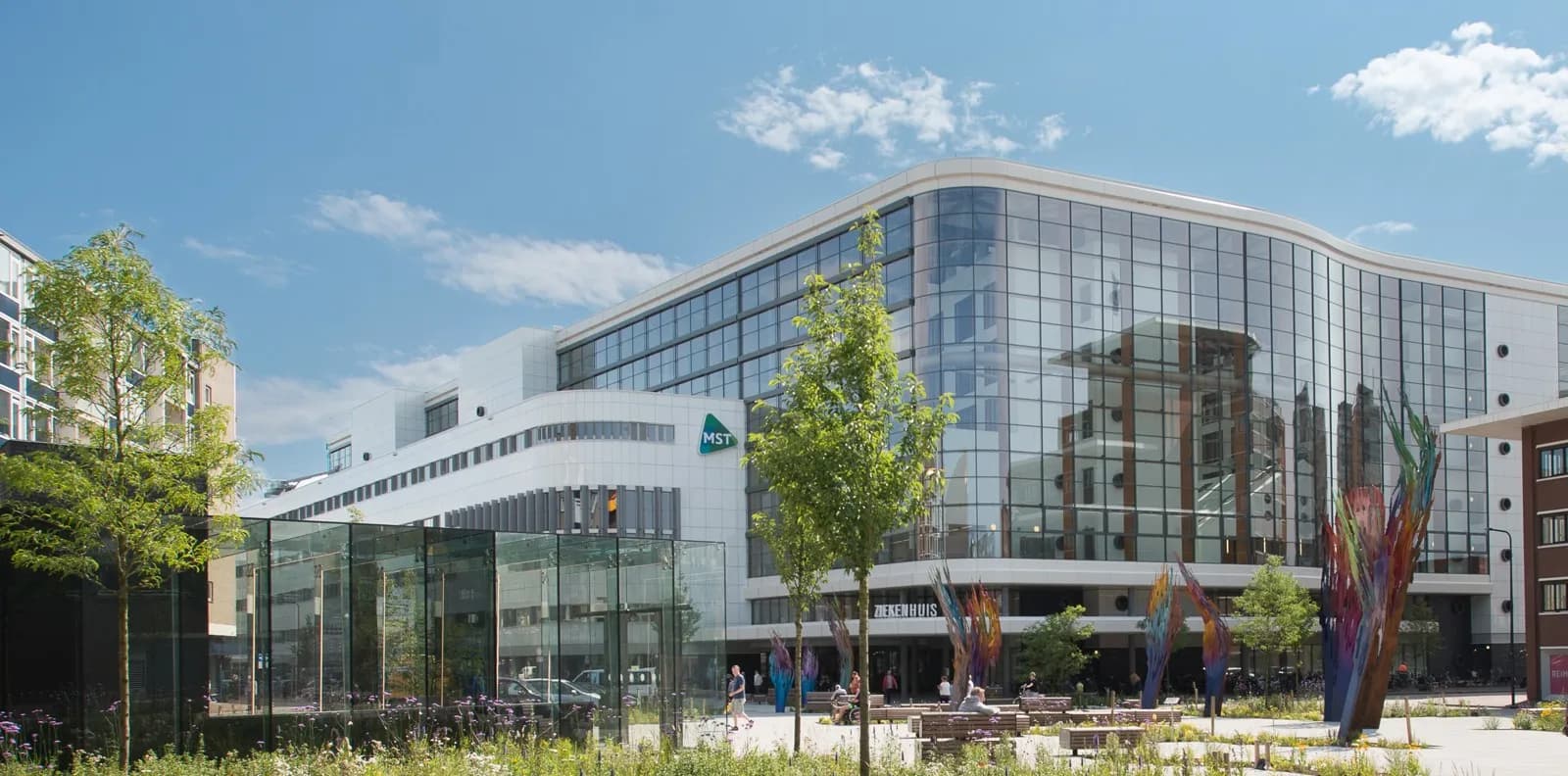 Glazen gevel van MST aan het Koningsplein in Enschede, met kunstwerken op het plein